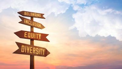 A crossroad sign with 4 arrows in front of a sunset. The 4 arrows read: Belonging, Inclusion, Equity, and Diversity