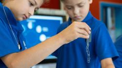 Two students stare intently at a magnet supporting a chain of paper clips