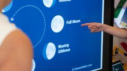 Students examine a chart of Earth's moon's cycle. A student points to Full Moon between Waning and Waxing Gibbous