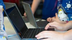 Students and a crocheted animal work on their laptops