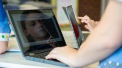 Students examine an 'Eyes on the Solar System' power point on their computer. One student's eye is reflectd next to Earth. 