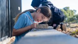 Two students make observations in a playground, one of a block of sandstone