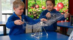 2 students drape cling film over a square based pyramid constructed of skewers and tape 