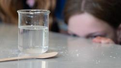 A student stares at a beaker holding a clear liquid. salt is spilt on the bench around the beaker