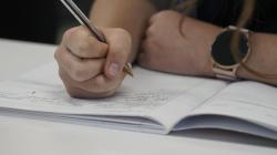 Close up on a student writing notes, pen clutched tightly 